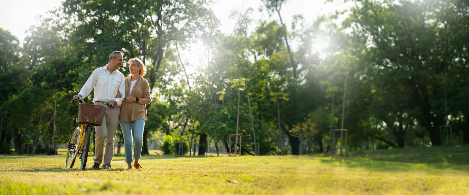 couple walking their bike along happily talking in park.