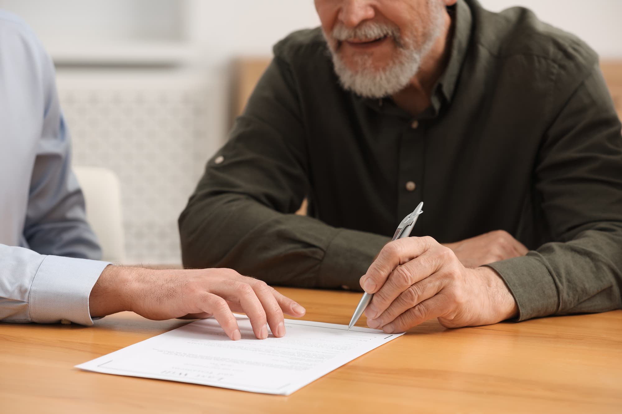 Notary showing senior man where to sign Last Will and Testament at wooden table indoors, closeup