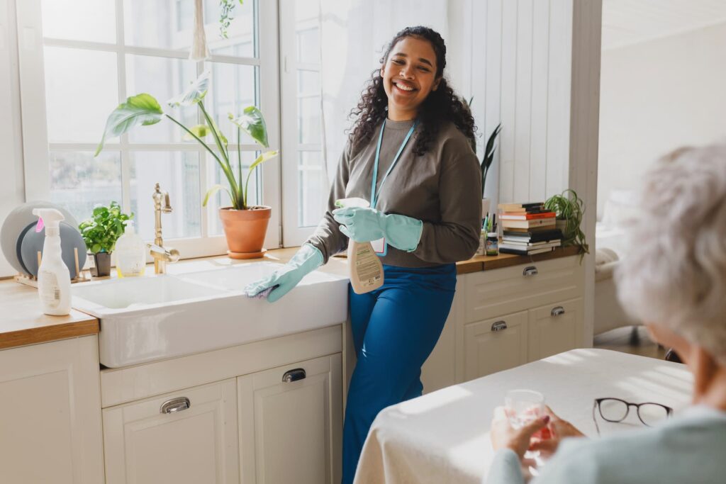 volunteer helping senior lady to clean house, standing in kitchen in raisin gloves washing sink with detergent