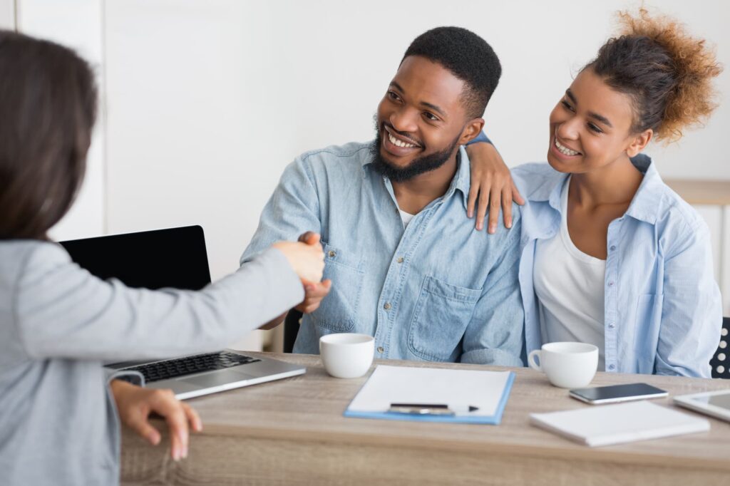 Smiling spouses handshaking with insurance broker in office