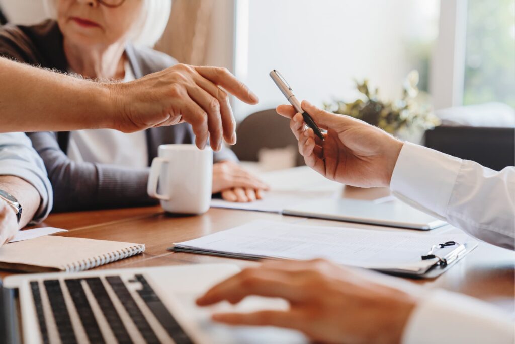Close up of 60s husband and wife sit at desk sign health insurance contract close deal, smiling old mature couple spouses put signature on document make good agreement, elderly healthcare concept