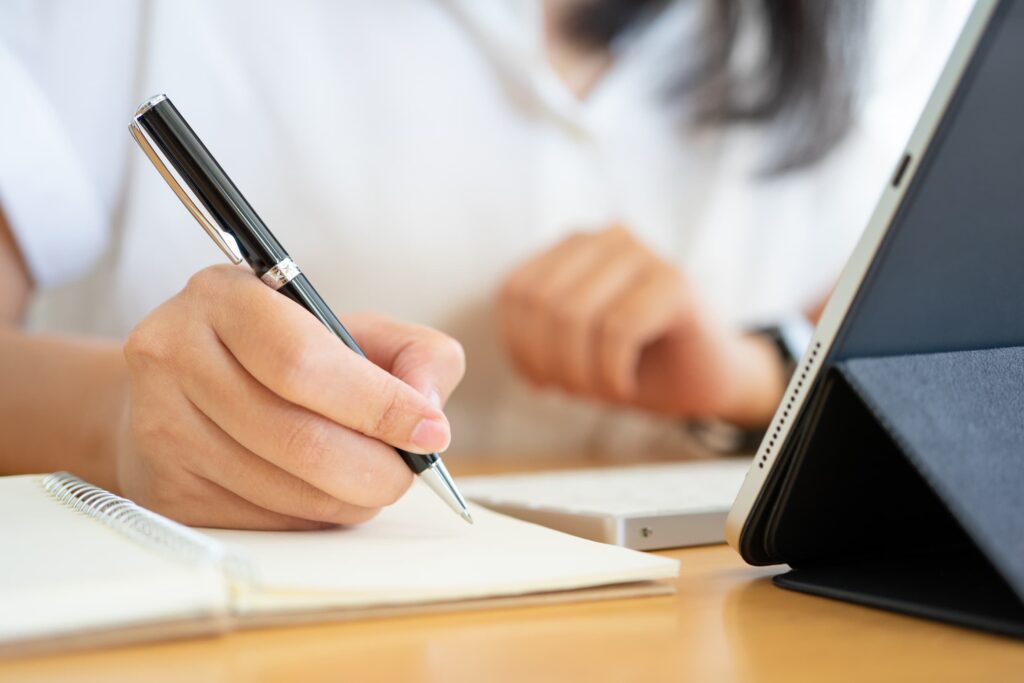 Close shot of businesswoman hands holding a pen writing something on the paper on the foreground in office.